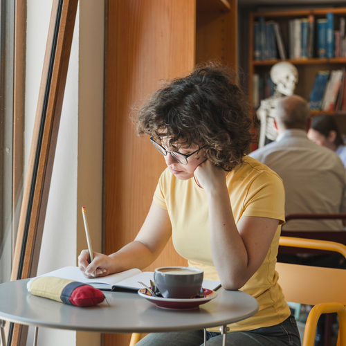 thoughtful-teen-girl-writing-notepad-near-window (1)